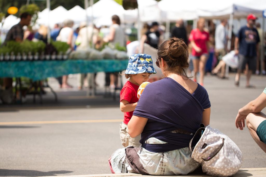 a mother talks to her toddler while babywearing her baby