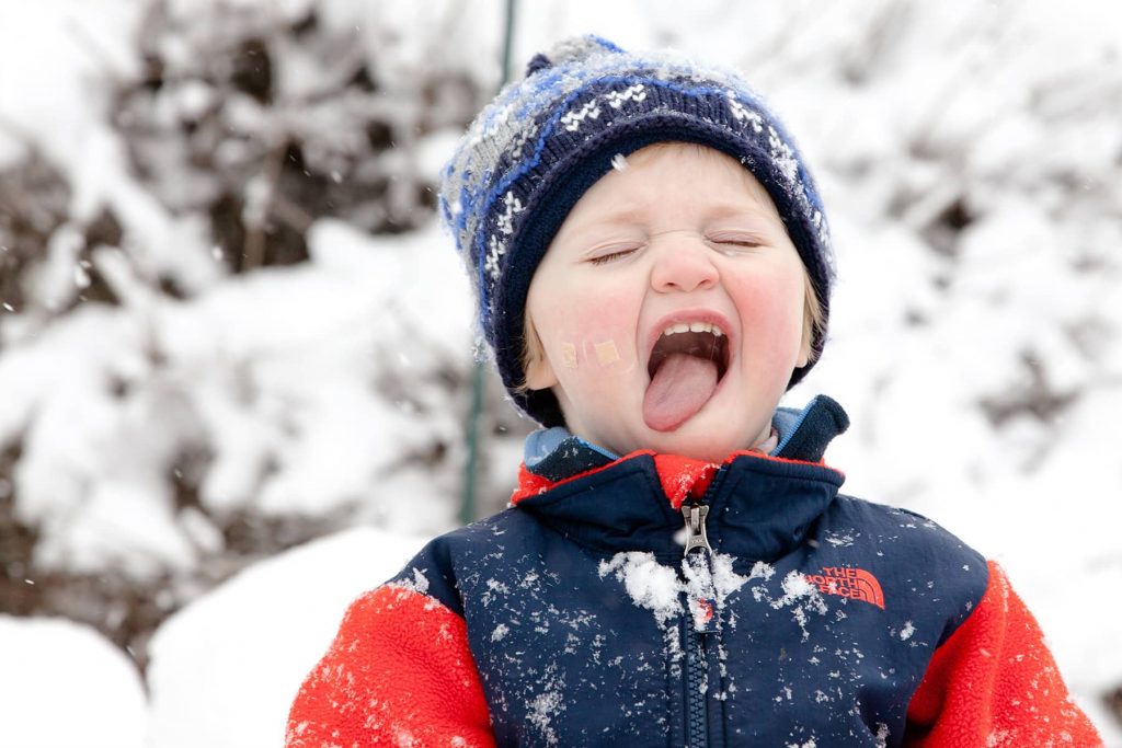 toddler boy catches snow on his tongue in the winter