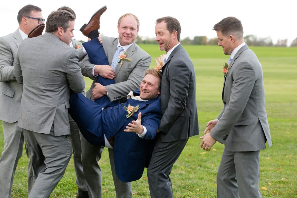 groomsmen pick the groom up and laugh
