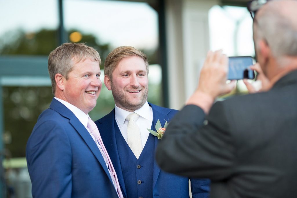 groom and friend pose for a picture from a cell phone