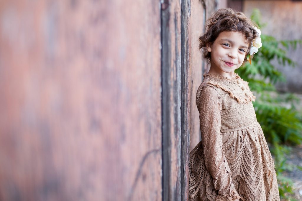 girl leaning against a rusty wall in a brown lace dress in Rochester NY