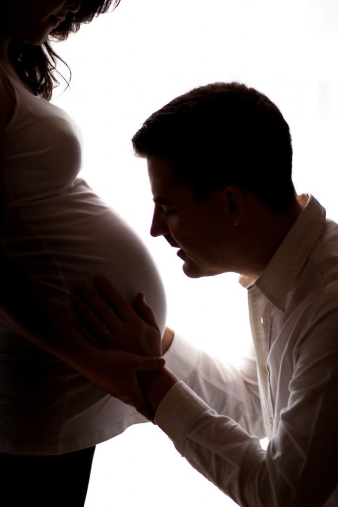 silhouette of a man kissing his unborn child in his wife's pregnant belly