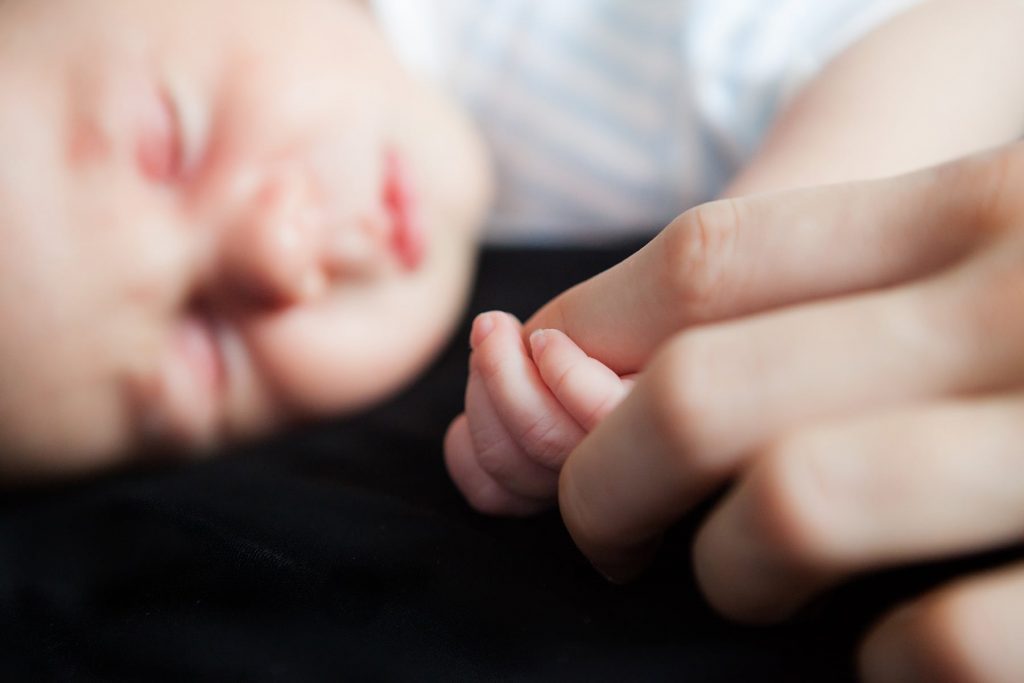 newborn sleeps while mother holds her finger
