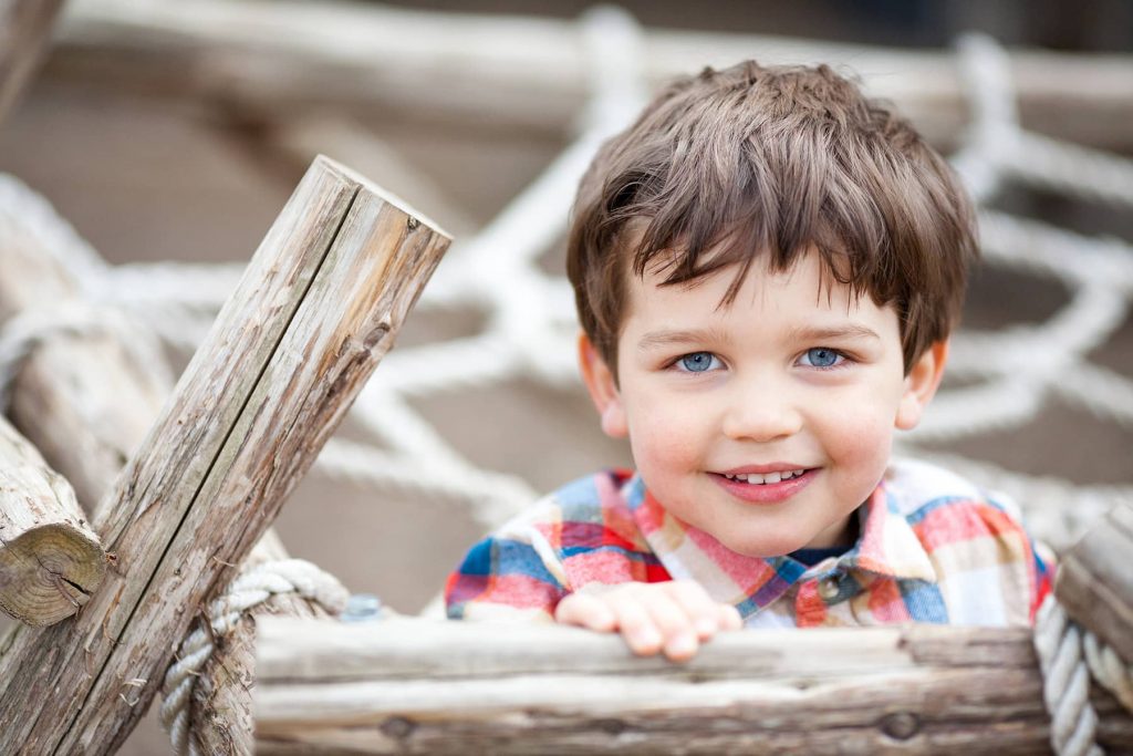 toddler-aged boy playing on jungle gym with blue eyes
