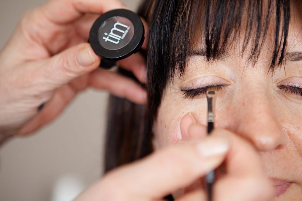 eye makeup is being applied to an eyelid of a woman in her 40s